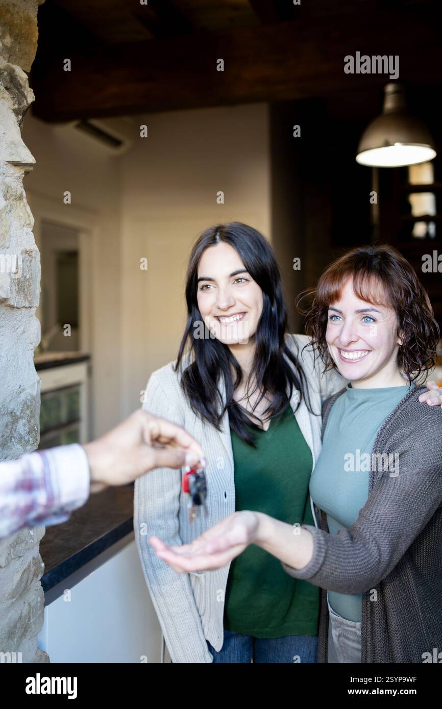 Due donne sorridenti LGTBI ricevono felicemente le chiavi della loro nuova casa, simboleggiando un nuovo inizio e nuovi inizi. stanno insieme alla porta, Foto Stock