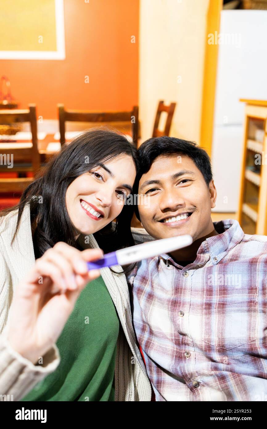 La coppia felice sorride mentre tiene un test di gravidanza positivo, condividendo l'emozione di aspettarsi un bambino. celebrano questo momento speciale insieme Foto Stock
