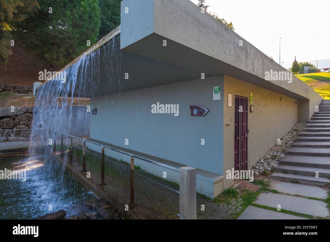 Una moderna struttura in cemento con cascata e scala adiacente in un parco Foto Stock