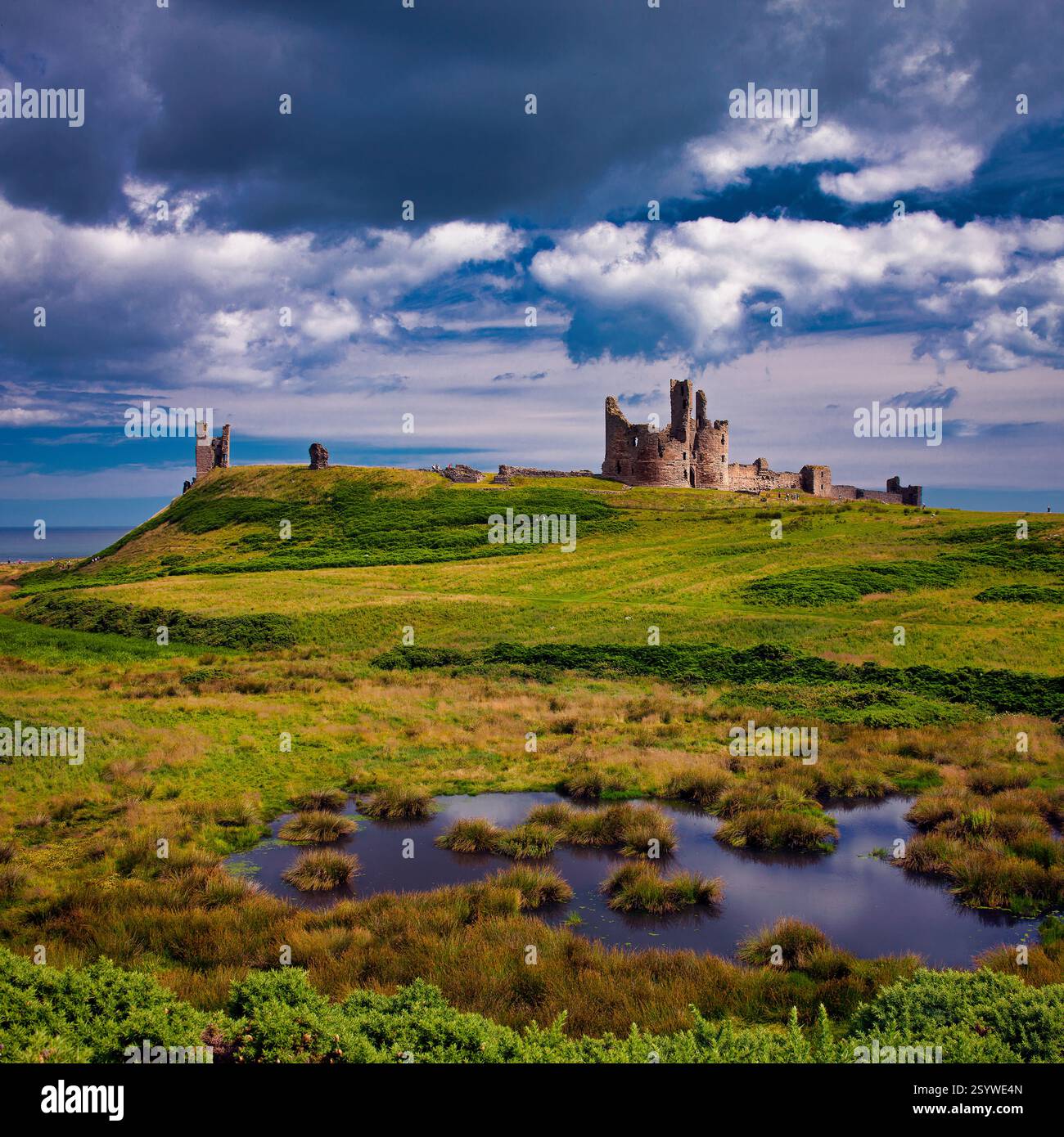 Ammira il castello di Dunstanburgh nel Northumberland, vicino a craster, in estate, in una giornata di sole, guardando verso Low Newton con incantevoli nuvole Foto Stock