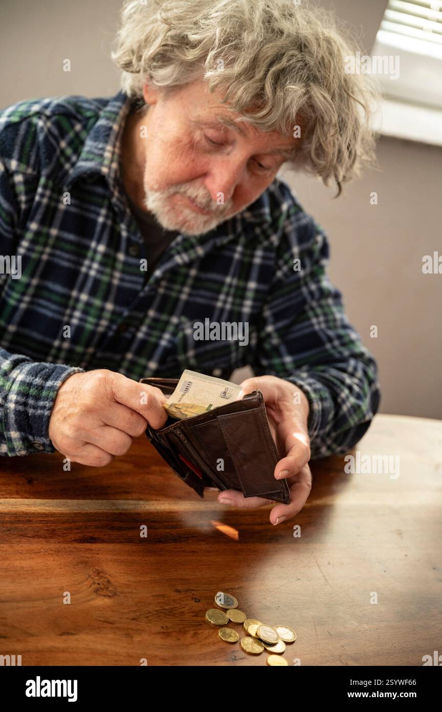 Un uomo anziano con i capelli grigi e una camicia a quadri guarda il portafoglio mentre conta i suoi soldi su un tavolo di legno. Foto Stock