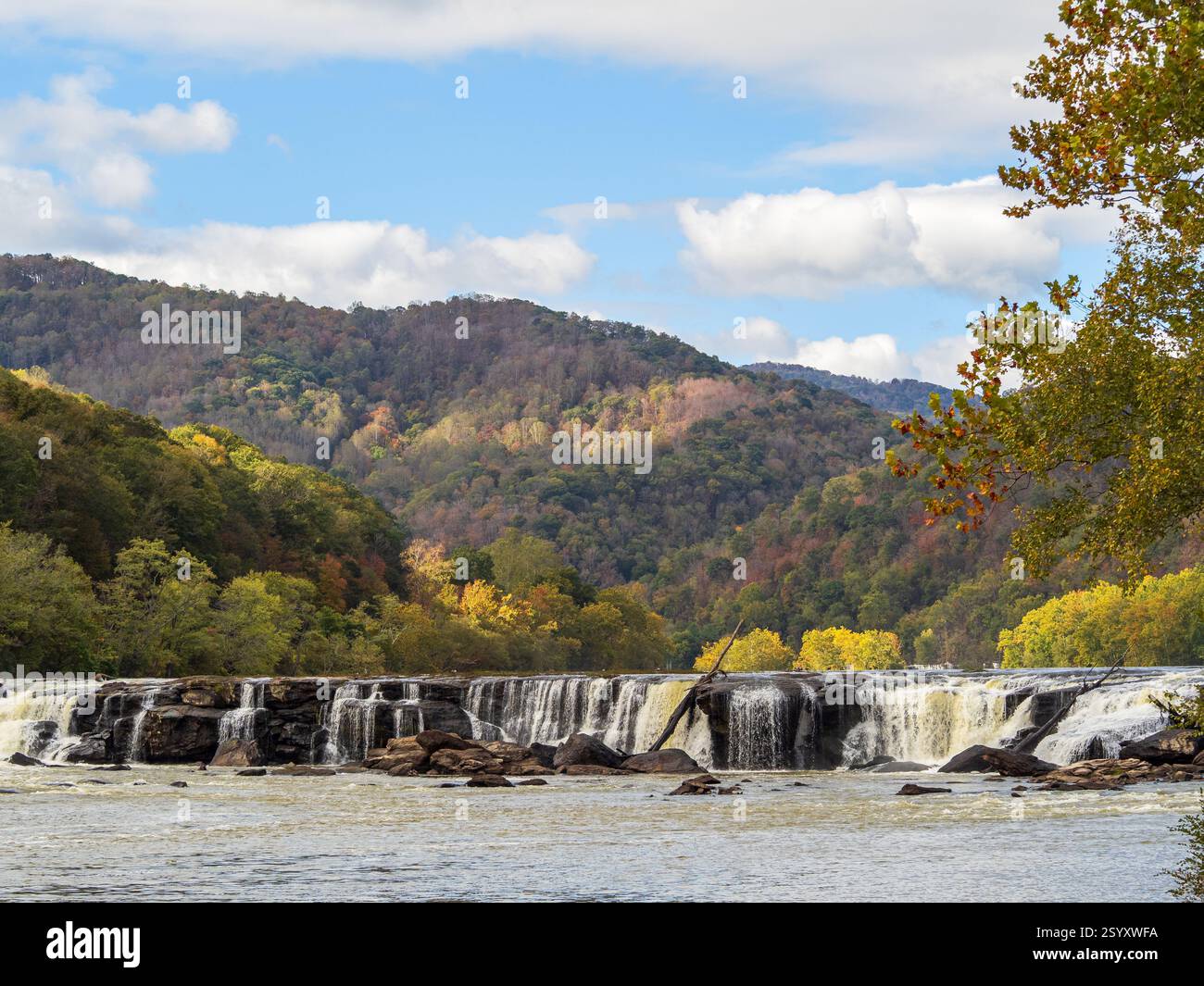 Le cascate Sandstone Falls, il New River Gorge National Park, West Virginia, si affacciano su brillanti colori autunnali sotto un cielo azzurro vivace, mentre i raggi del sole fanno il bagno Foto Stock