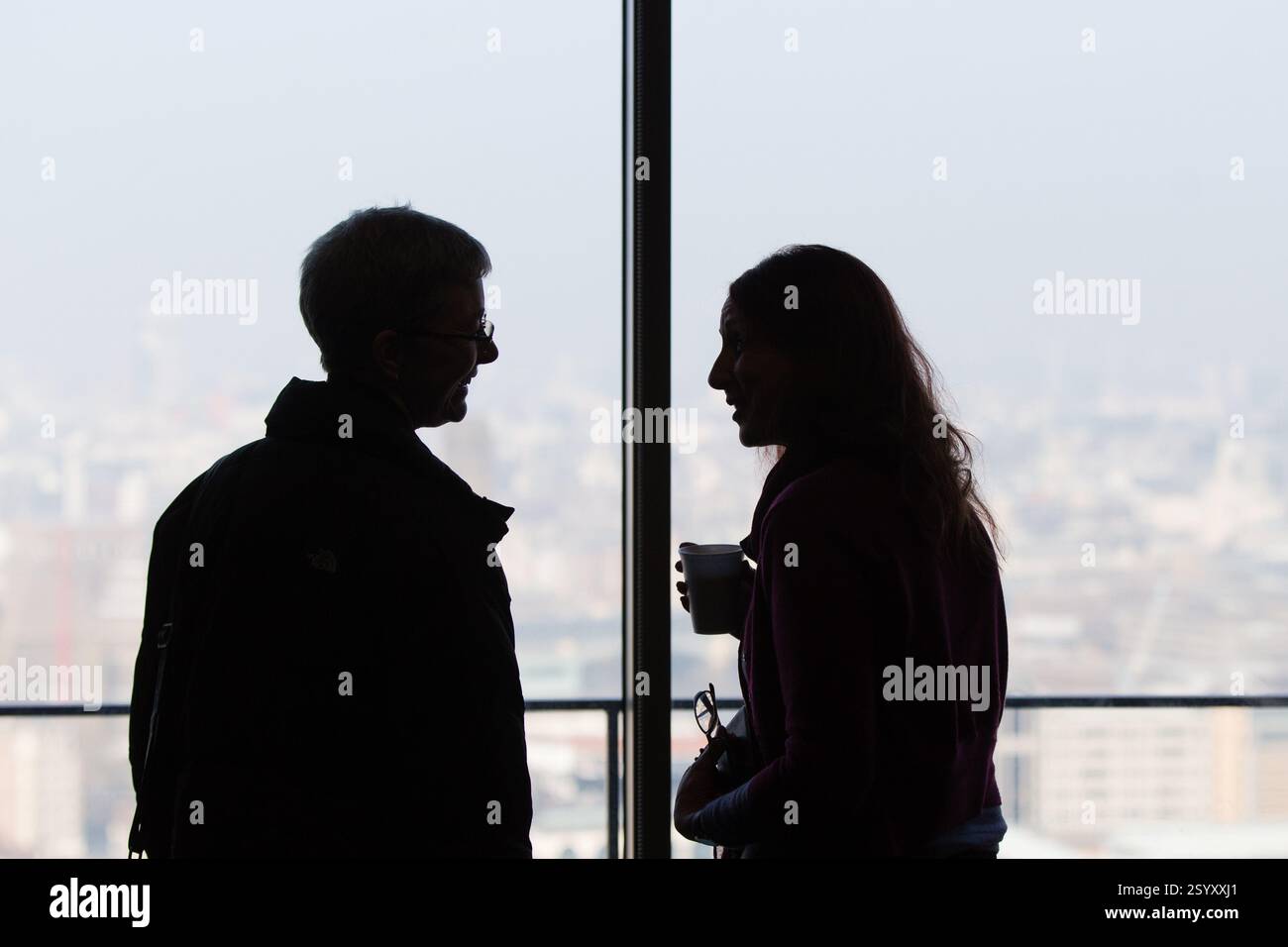 Due persone, che probabilmente hanno una conversazione, stanno davanti a una finestra che si affaccia sulla città Foto Stock