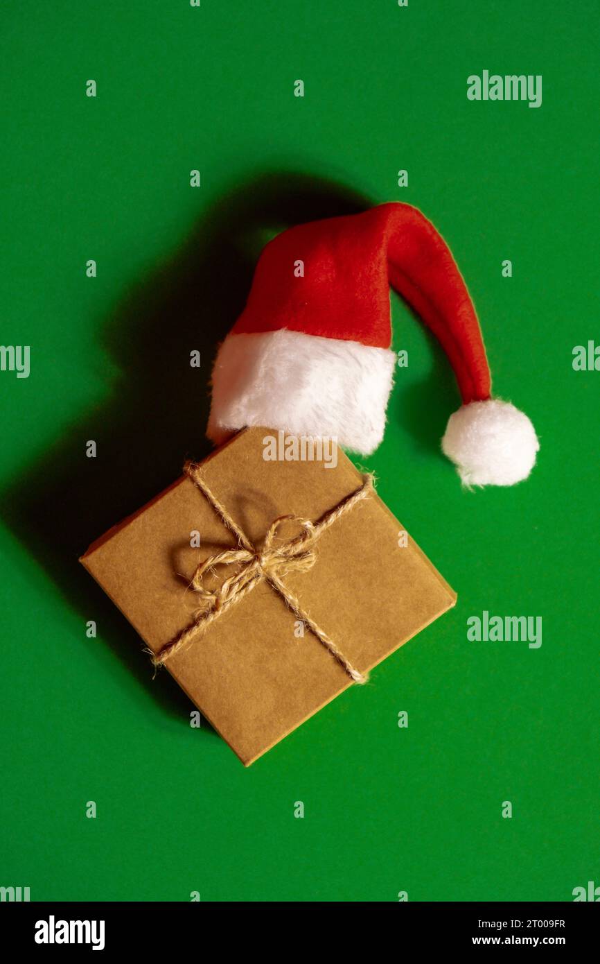 Cappello di Babbo Natale su scatola regalo di carta presente su sfondo verde. Spazio di copia per il testo. Fai il mock-up per la pubblicità. Natale natalizio Foto Stock