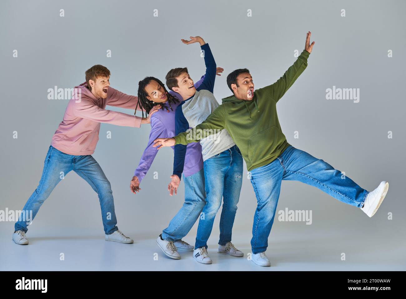 quattro amici allegri in abiti vivaci e informali che si divertono su sfondo grigio, diversità culturale Foto Stock