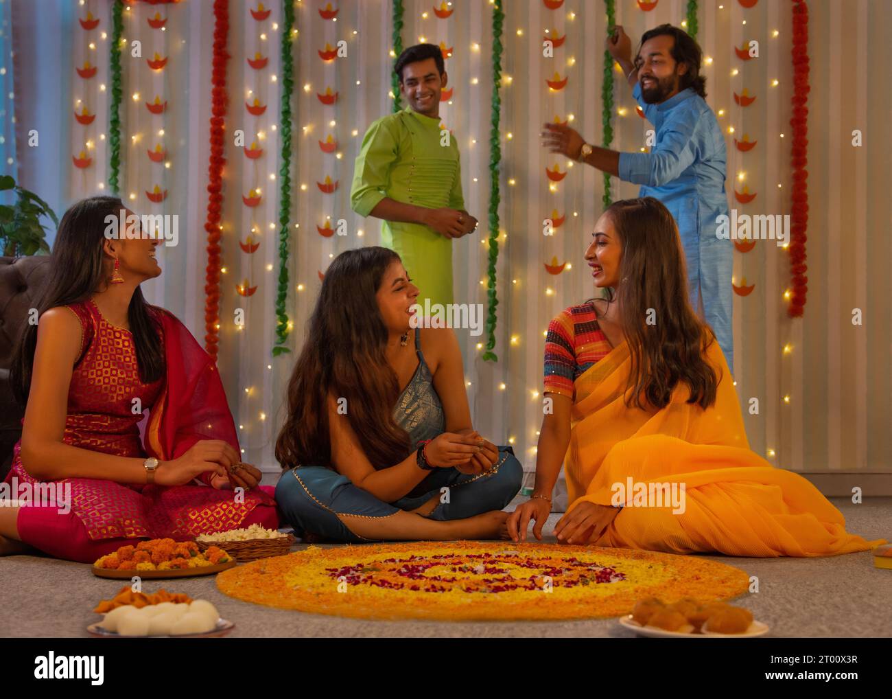 Gli amici si divertono mentre decorano il pavimento con fiori ( Rangoli) in occasione di Diwali Foto Stock