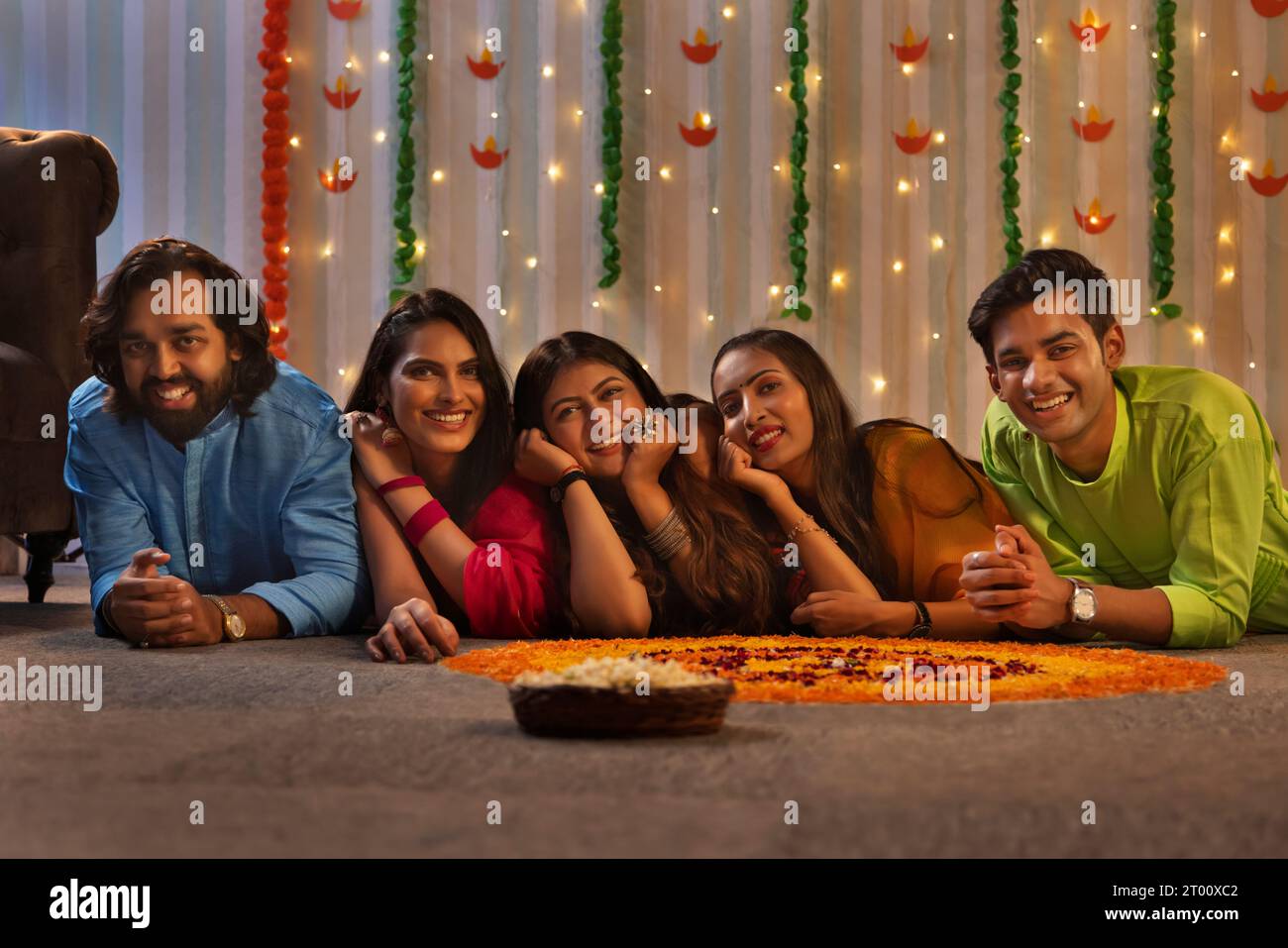 Amici che si trovano sul pavimento vicino alla decorazione floreale durante la celebrazione Diwali Foto Stock