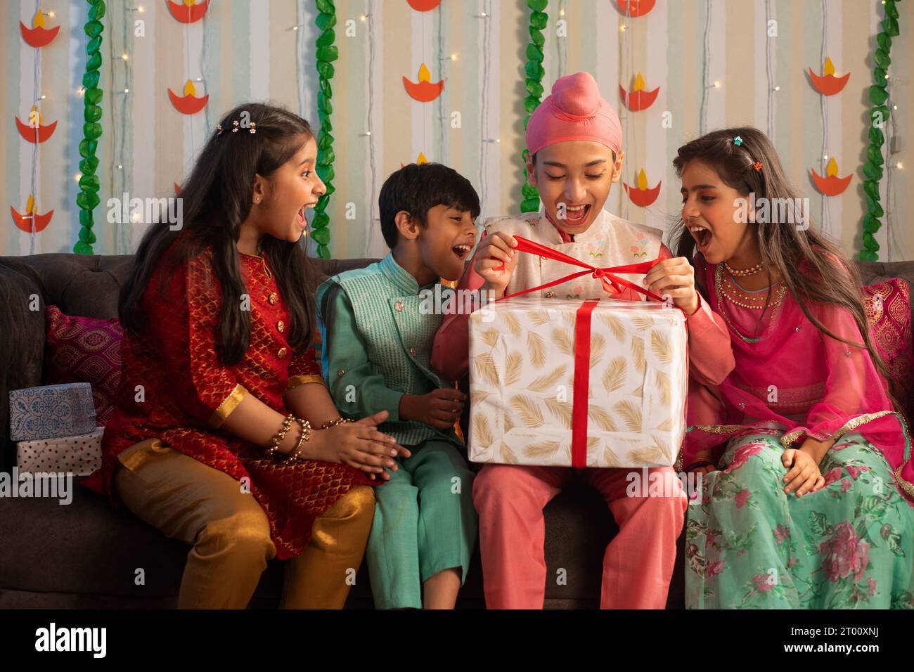 Gruppo di bambini seduti su un divano, apertura della confezione regalo durante le celebrazioni Diwali Foto Stock