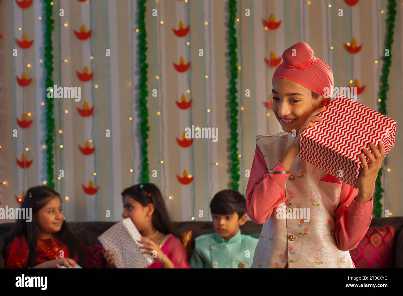 Ragazzo Sikh in piedi con un regalo in occasione di Diwali e dei suoi amici seduti dietro Foto Stock