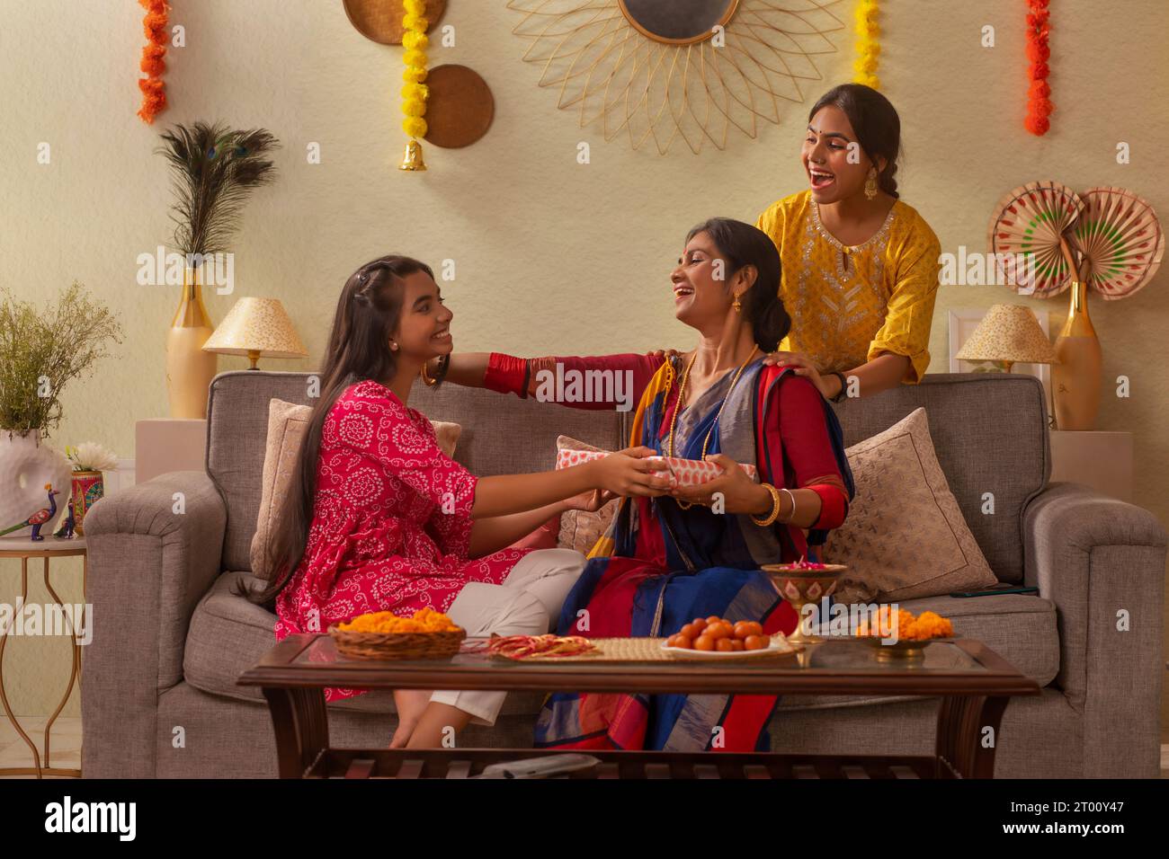 Famiglia bengalese che si scambia un regalo mentre si siede insieme sul divano in soggiorno in occasione della Durga Puja Foto Stock