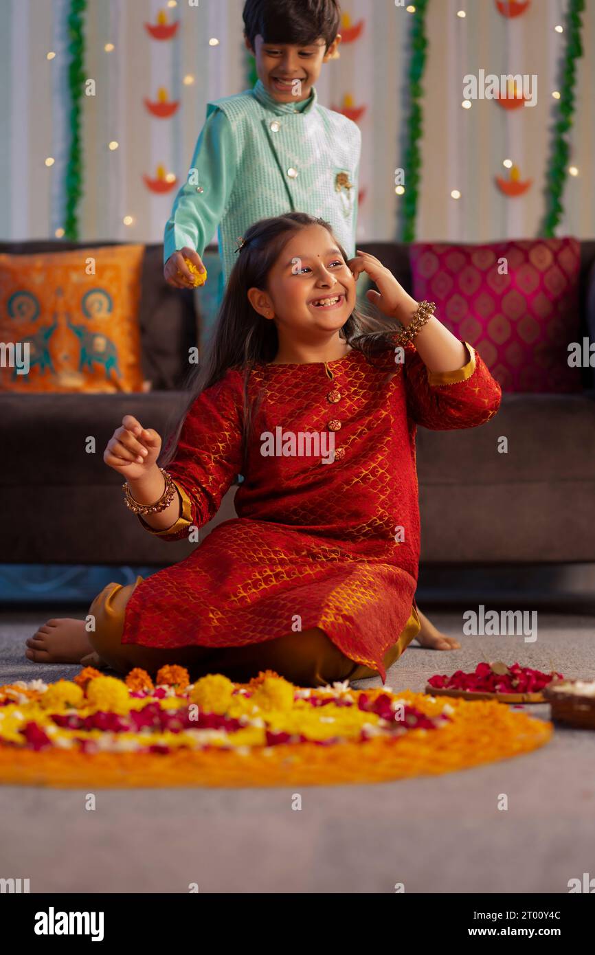 Ragazza che fa rangoli floreali in occasione di Diwali e ragazzo in piedi dietro Foto Stock