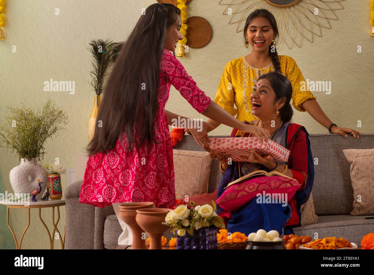 Famiglia bengalese che si scambia un regalo mentre si siede insieme sul divano in soggiorno in occasione della Durga Puja Foto Stock