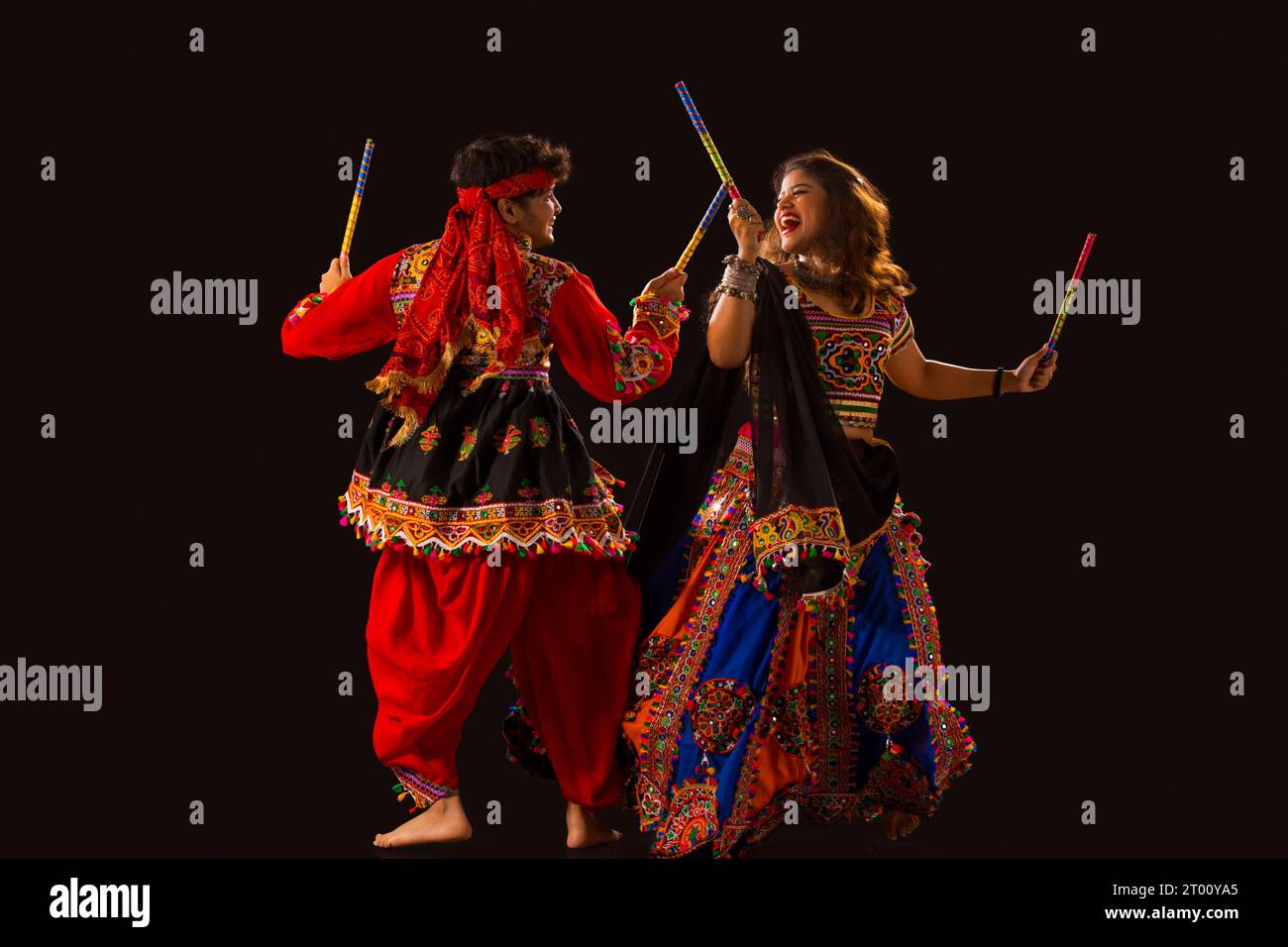Una giovane coppia felice che esegue Dandiya Raas su sfondo nero, durante le celebrazioni di Navratri Foto Stock