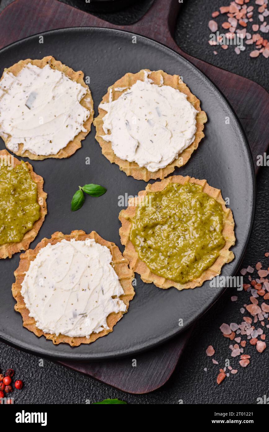 Spuntini rotondi con patatine fritte o cracker croccanti con formaggio cremoso e pesto su un piatto di ceramica Foto Stock