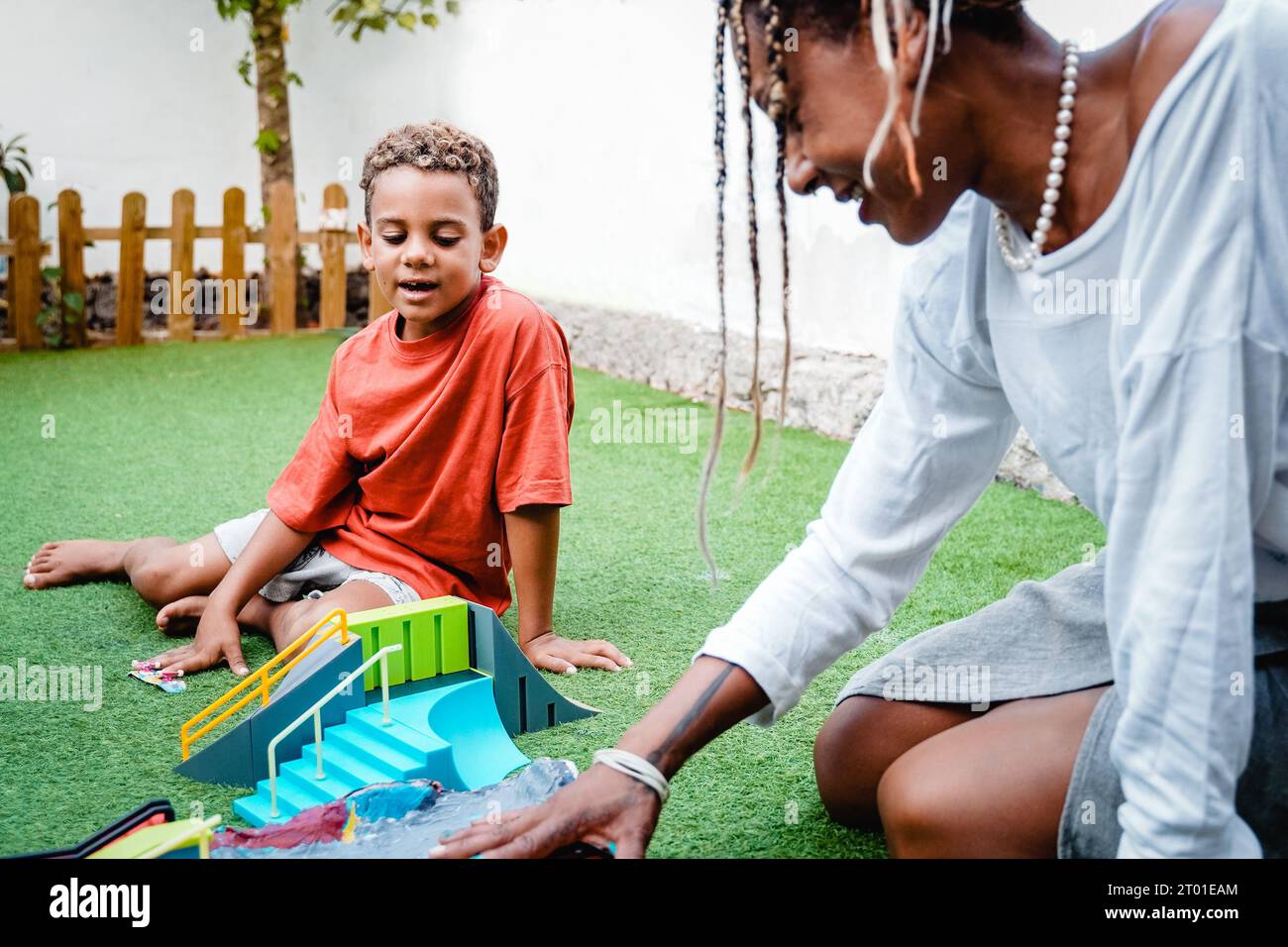 Mamma e figlio africani felici che giocano con i giocattoli da skateboard all'aperto sulla terrazza della casa - rapporto di famiglia, concetto di stile di vita amoroso Foto Stock