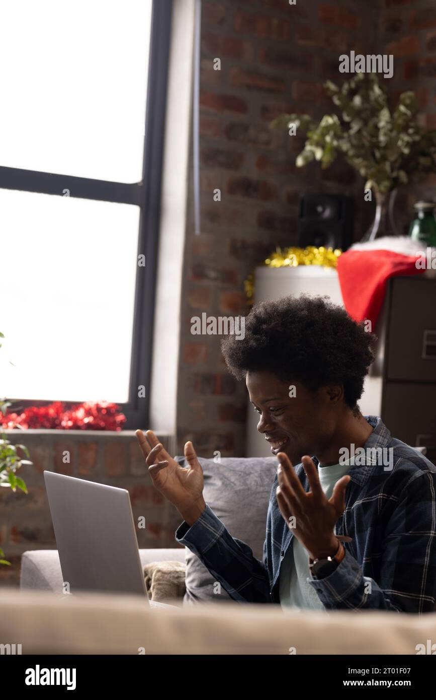 Felice afro-americano che effettua una videochiamata su un computer portatile seduto a casa durante il periodo natalizio, spazio per le copie Foto Stock
