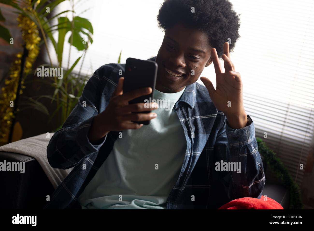 Felice uomo afroamericano con videochiamata su smartphone, seduto a casa nel periodo natalizio Foto Stock