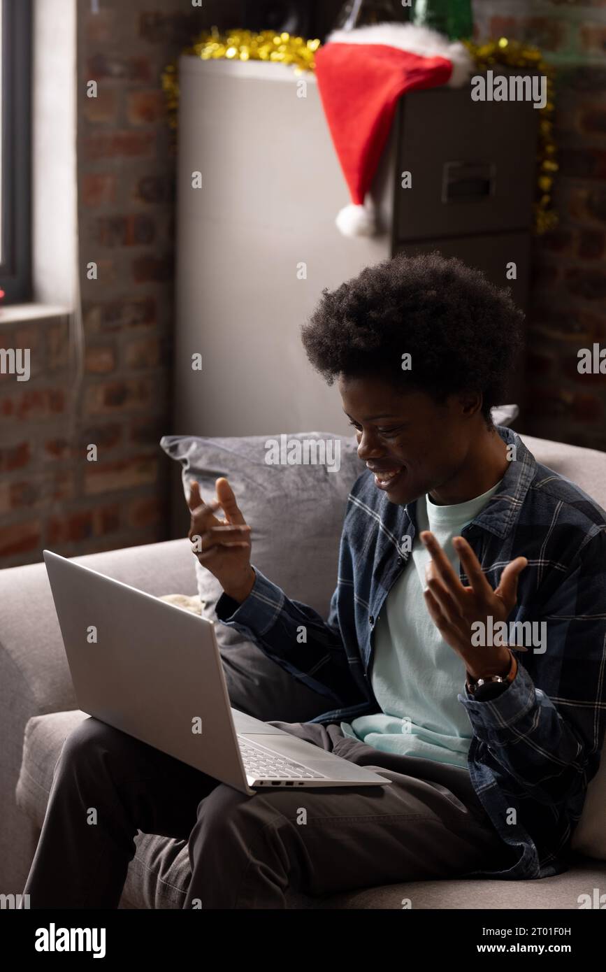 Felice afro-americano che effettua una videochiamata su un computer portatile seduto a casa durante il periodo natalizio, spazio per le copie Foto Stock