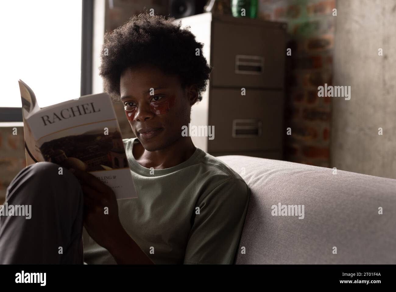 Uomo afroamericano concentrato seduto sul divano leggendo un libro con maschere per gli occhi, spazio per le copie Foto Stock