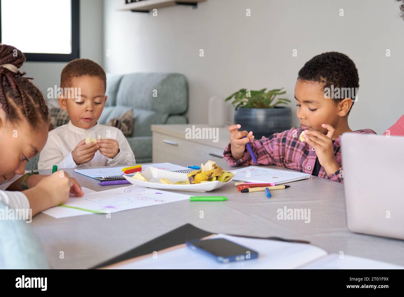 Tre bambini che fanno uno spuntino mentre dipingono o fanno i compiti a casa. Foto Stock