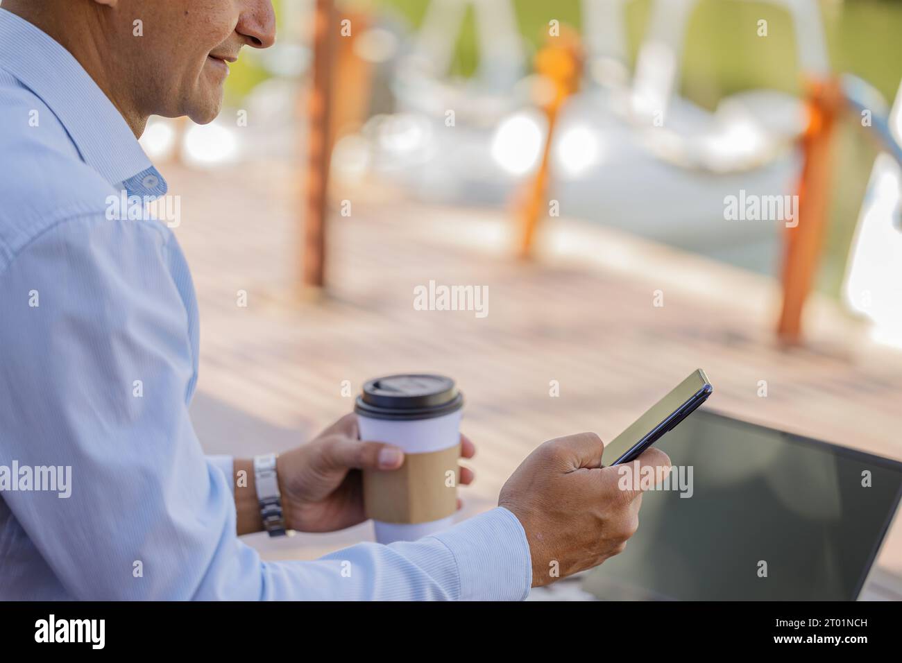 Dettaglio delle mani di un uomo latino che tiene un telefono cellulare e una tazza usa e getta con caffè. Foto Stock