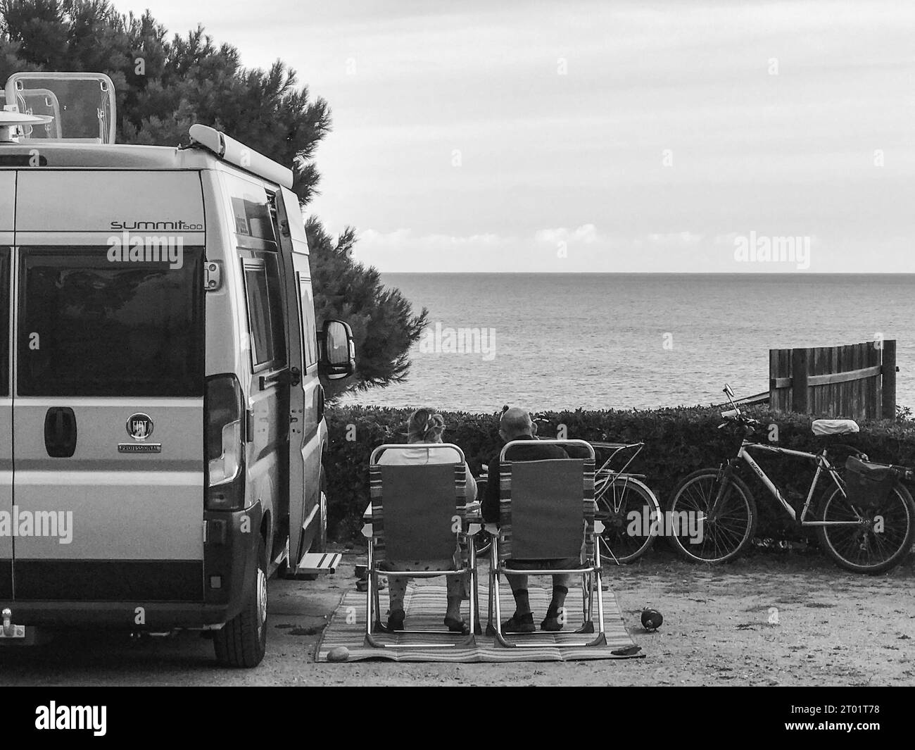 Campeggio panoramico per camper, camper nel parco di veicoli ricreativi, donne e uomini che si rilassano su una sedia e guardano il tramonto sul mare Foto Stock
