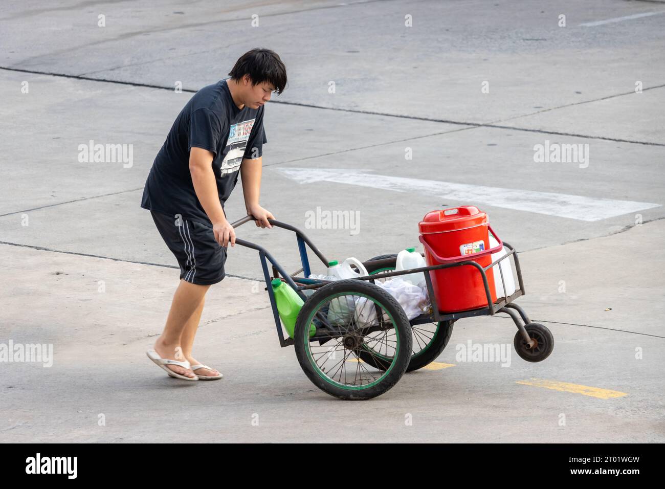 SAMUT PRAKAN, THAILANDIA, 25 2023 settembre, Un uomo spinge un carro a tre ruote con un carico Foto Stock