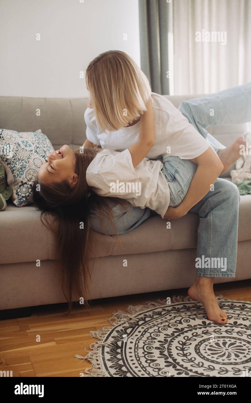 Felice giovane e attraente madre che si tiene per mano una simpatica figlia sorridente seduta sul divano a casa. Ravvicinati i genitori che si divertono a giocare e a divertirsi Foto Stock