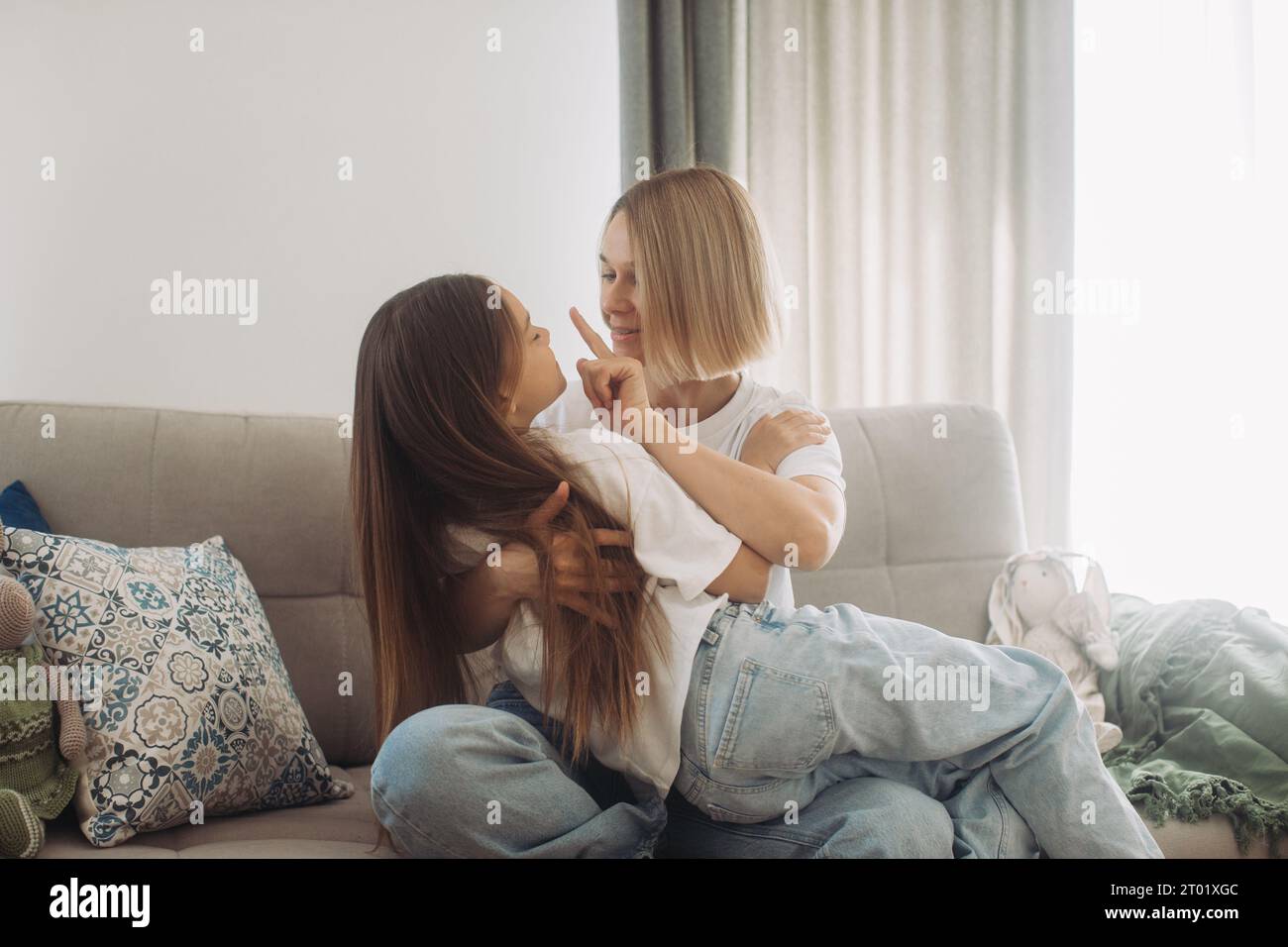 Felice giovane e attraente madre che si tiene per mano una simpatica figlia sorridente seduta sul divano a casa. Ravvicinati i genitori che si divertono a giocare e a divertirsi Foto Stock