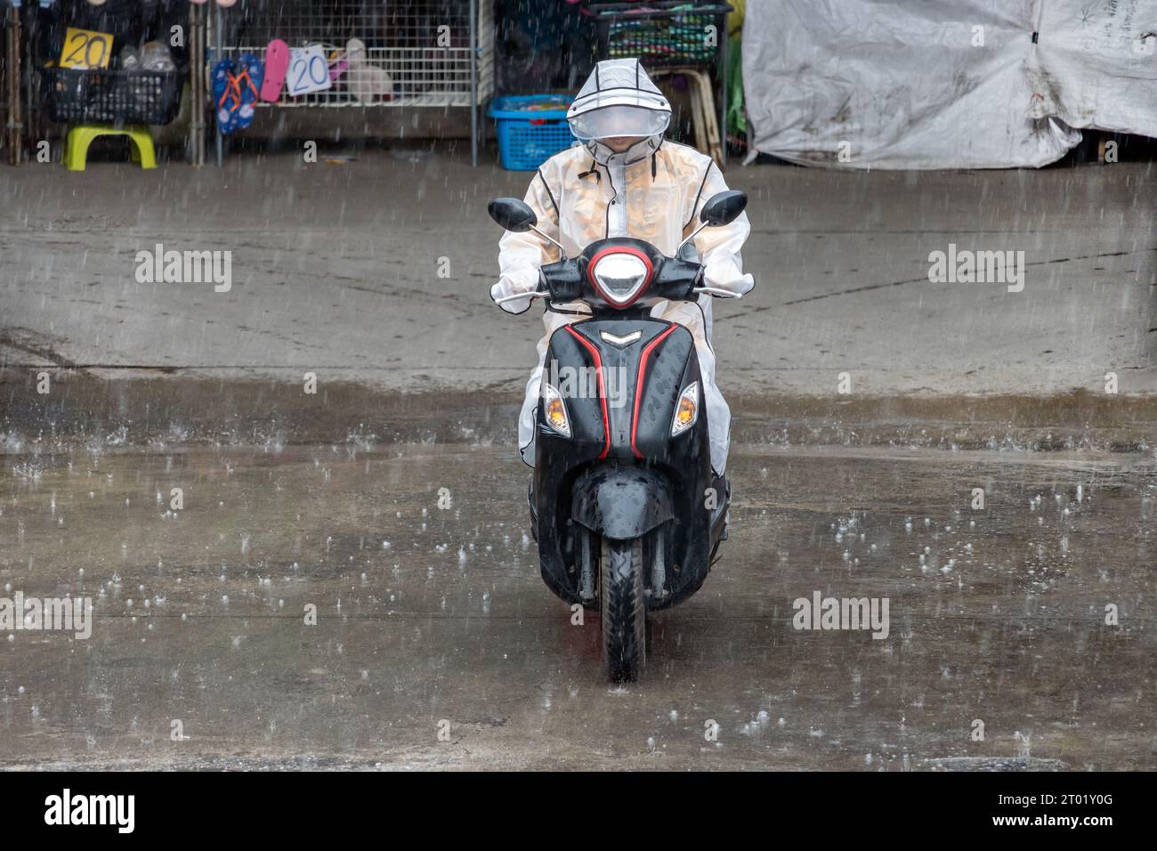 Un motociclista vestito con un impermeabile cavalca una moto sotto la pioggia, in Thailandia Foto Stock