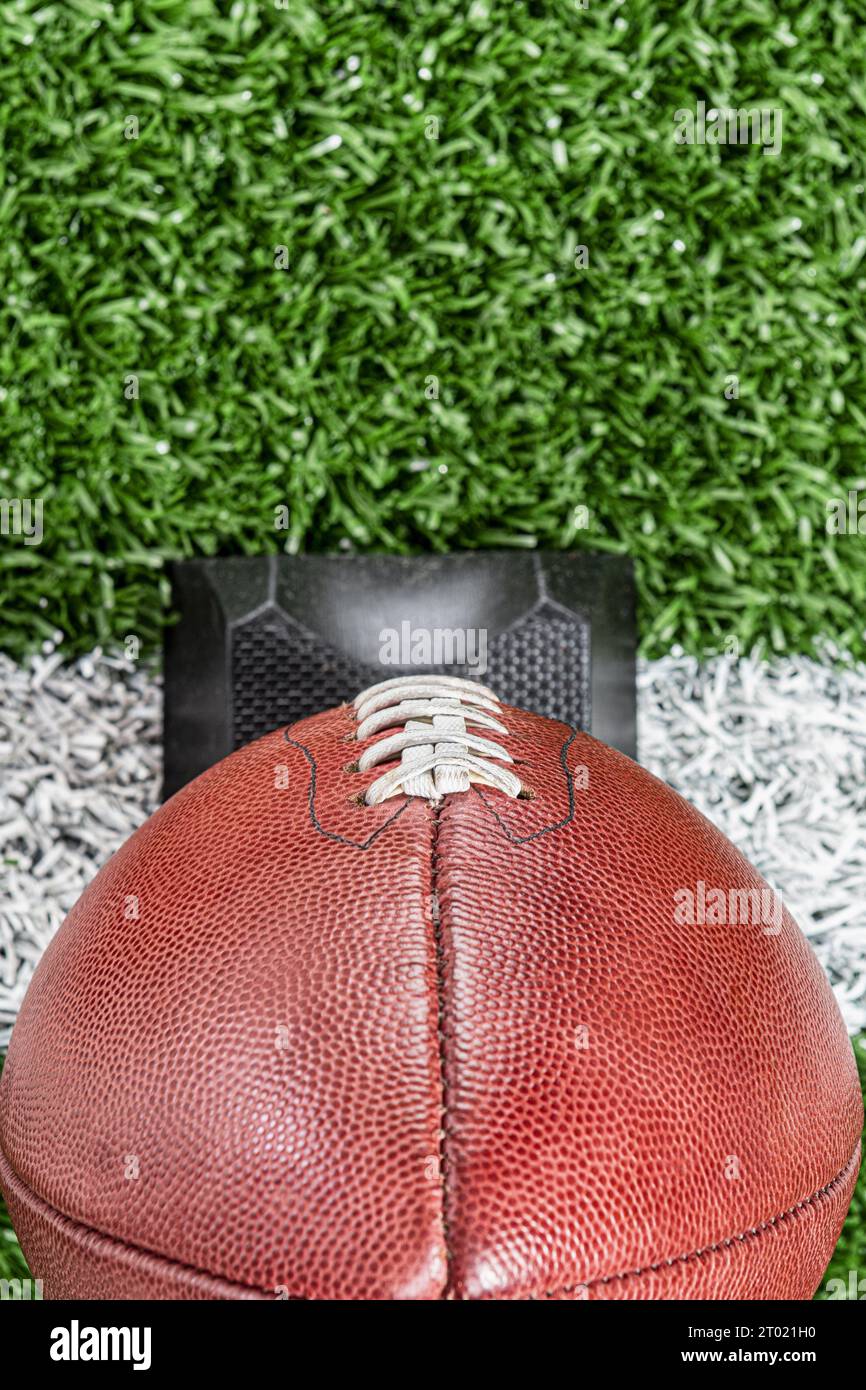 Un primo piano in alto di un football americano professionista in pelle, seduto su una maglietta nera che si trova su una linea bianca del campo di erba sintetica. Foto Stock