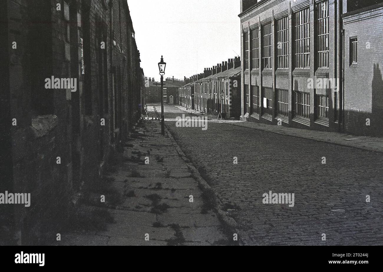 1960s, Historical, strada acciottolata al largo di Silver Street, Oldham, Machester, Inghilterra, Regno Unito, con case vittoriane a schiera e magazzino. Foto Stock