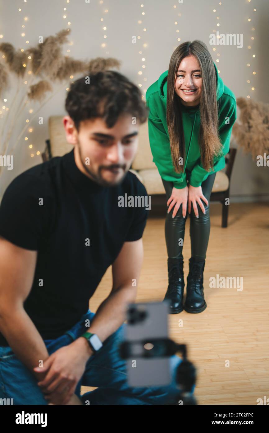 Giovane uomo e ragazza che guardano il video che hanno girato insieme per un post su Internet. Creazione di contenuti per i social network, utilizzando lo smartphone sul cavalletto in Foto Stock