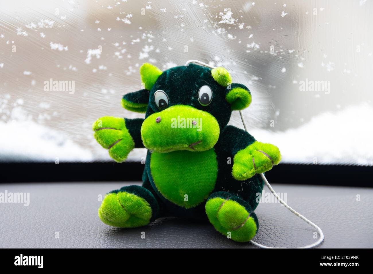 Mucca giocattolo verde seduta sul cruscotto di un'auto mentre la nuvola Foto Stock