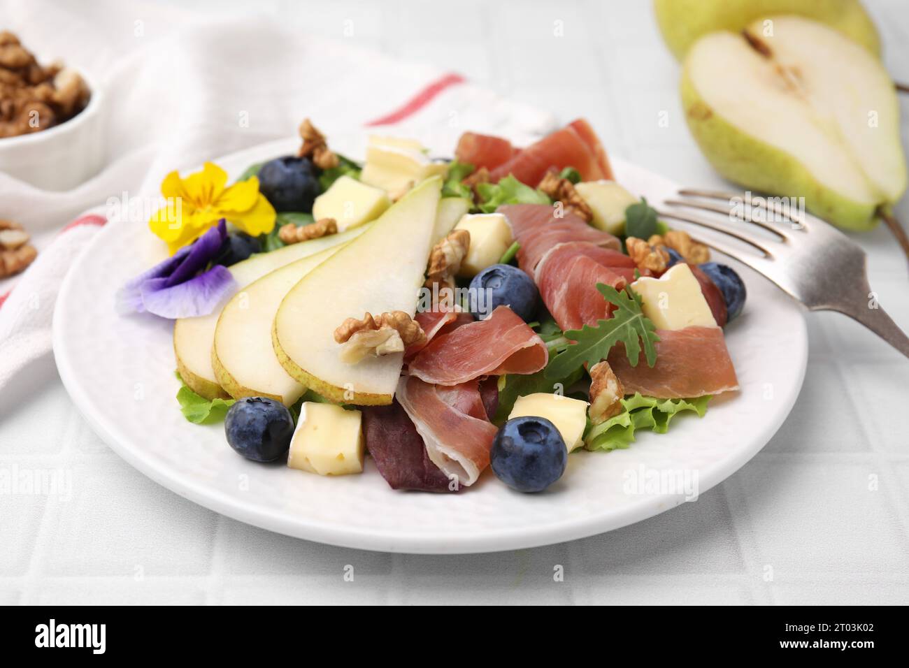 Insalata gustosa con formaggio brie, prosciutto, noci e pera su tavola piastrellata bianca, primo piano Foto Stock