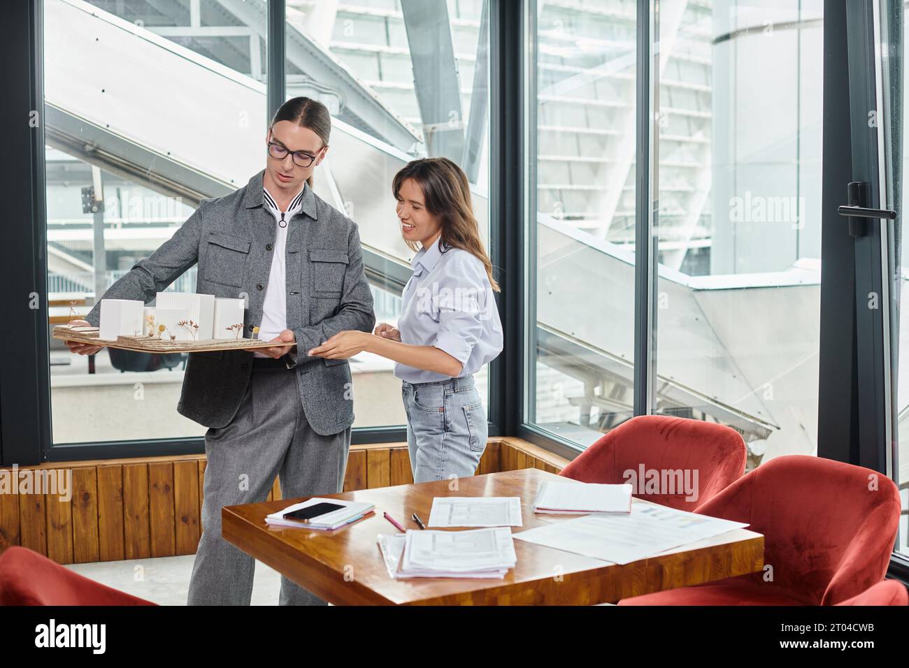 due giovani e ambiziosi colleghi che guardano il loro modello in scala con i documenti sul tavolo, ufficio di design Foto Stock