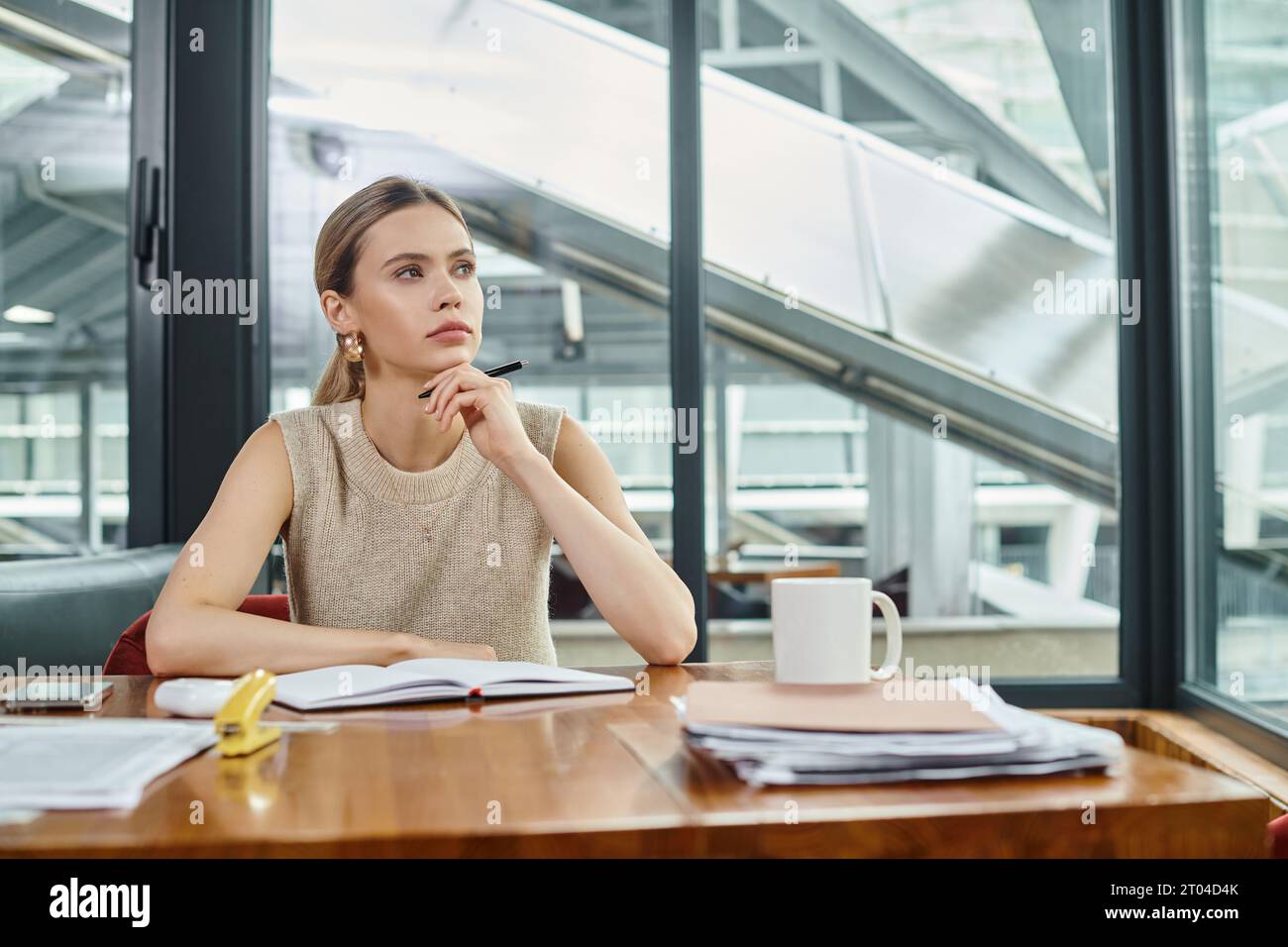 donna premurosa in abiti eleganti seduta al tavolo che lavora su documenti, mano al mento, coworking Foto Stock