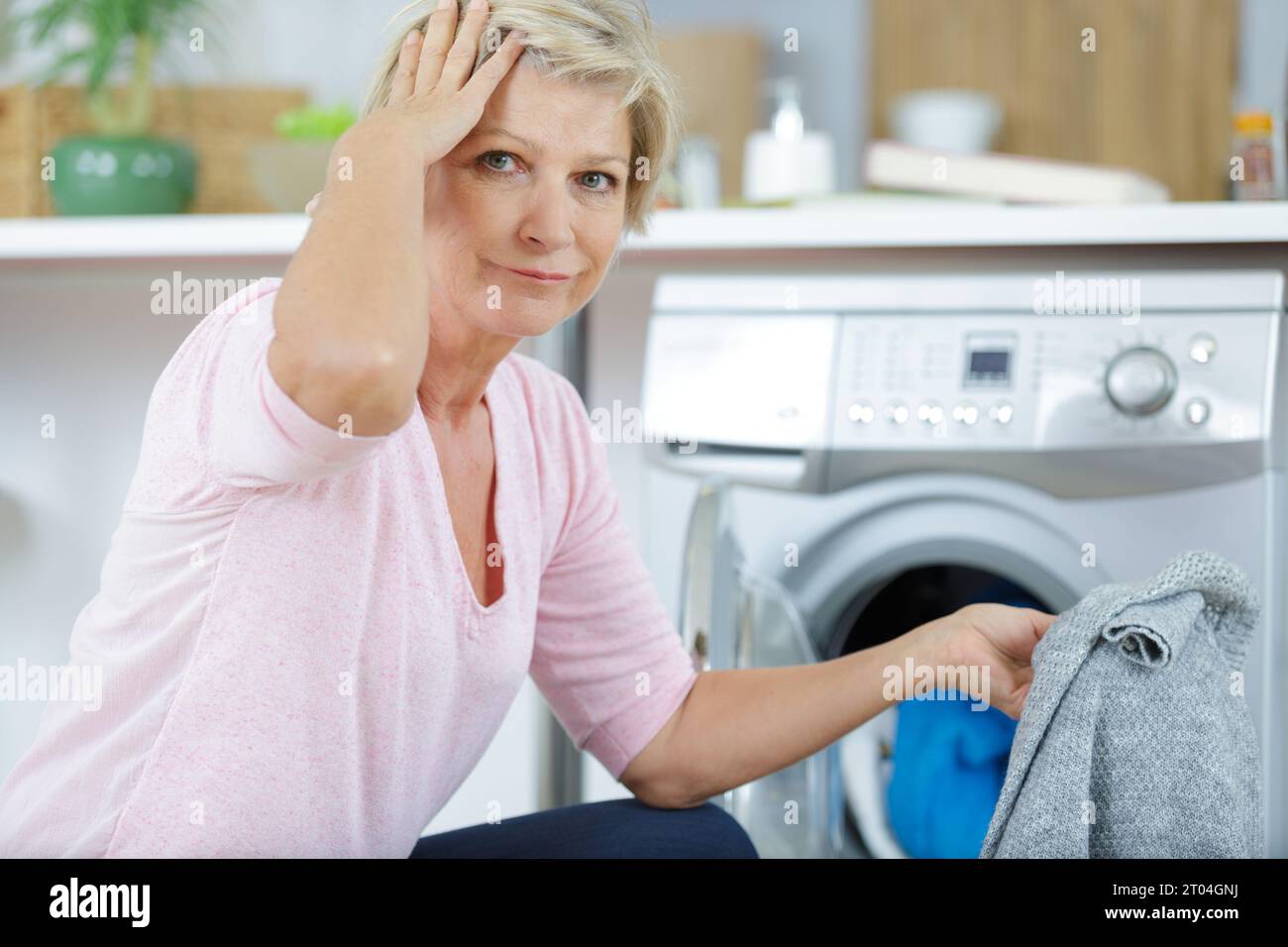donna matura dimenticata con la lavatrice che tiene il maglione Foto Stock