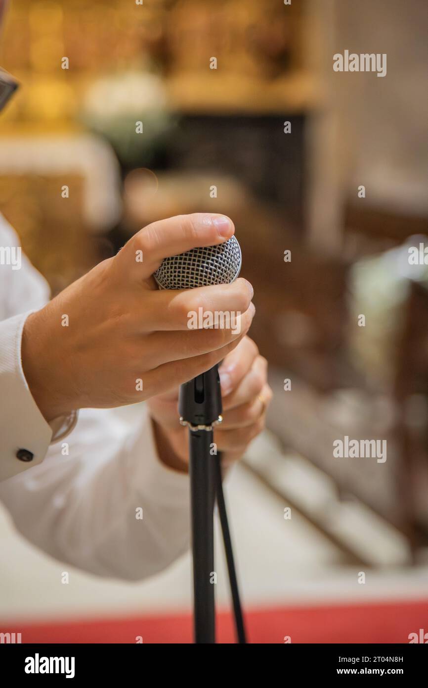 Uomo che tiene in mano e prepara il microfono da utilizzare nelle prestazioni musicali. Ambiente interno rustico, ad esempio tempio o chiesa. Primo piano Foto Stock