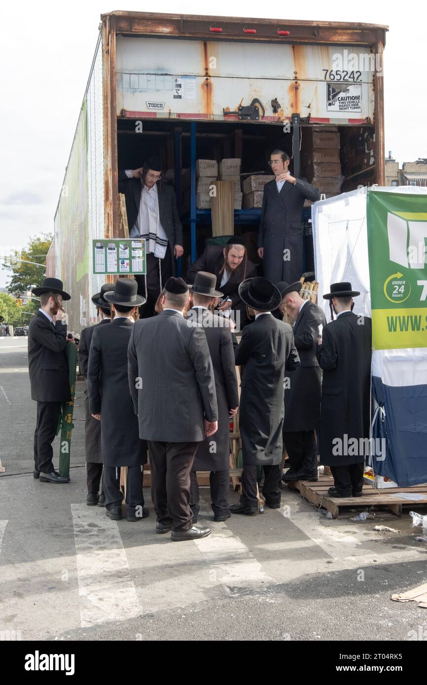 Un gruppo di ebrei ortodossi si trova accanto a un grande tappeto in attesa di comprare dei Sukkah prefabbricati e di farlo da soli. A Williamsburg, Brooklyn, New York. Foto Stock