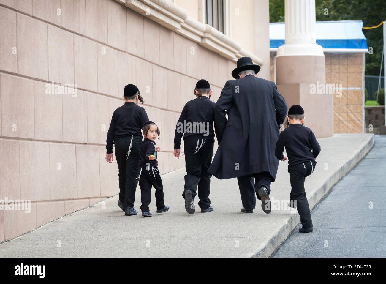 Un padre e i suoi 4 figli vestiti identicamente camminano su una pendenza per partecipare a un servizio sinagogico. A Kiryas Joel, Orange County, New York. Foto Stock