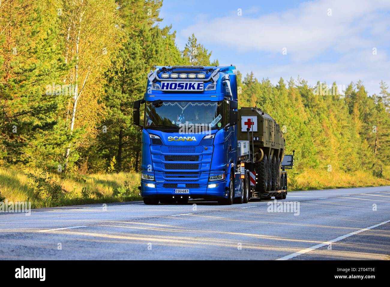 Blue Scania S500 Truck Hosike trasporta un veicolo di soccorso militare della Croce Rossa su un rimorchio con caricatore basso il giorno dell'autunno. Raasepori, Finlandia. 22 settembre 2023. Foto Stock