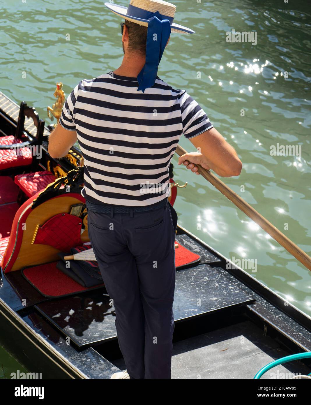 Vista posteriore di un gondoliere in una gondola nel canale di Venezia mentre percorre un romantico percorso turistico Foto Stock