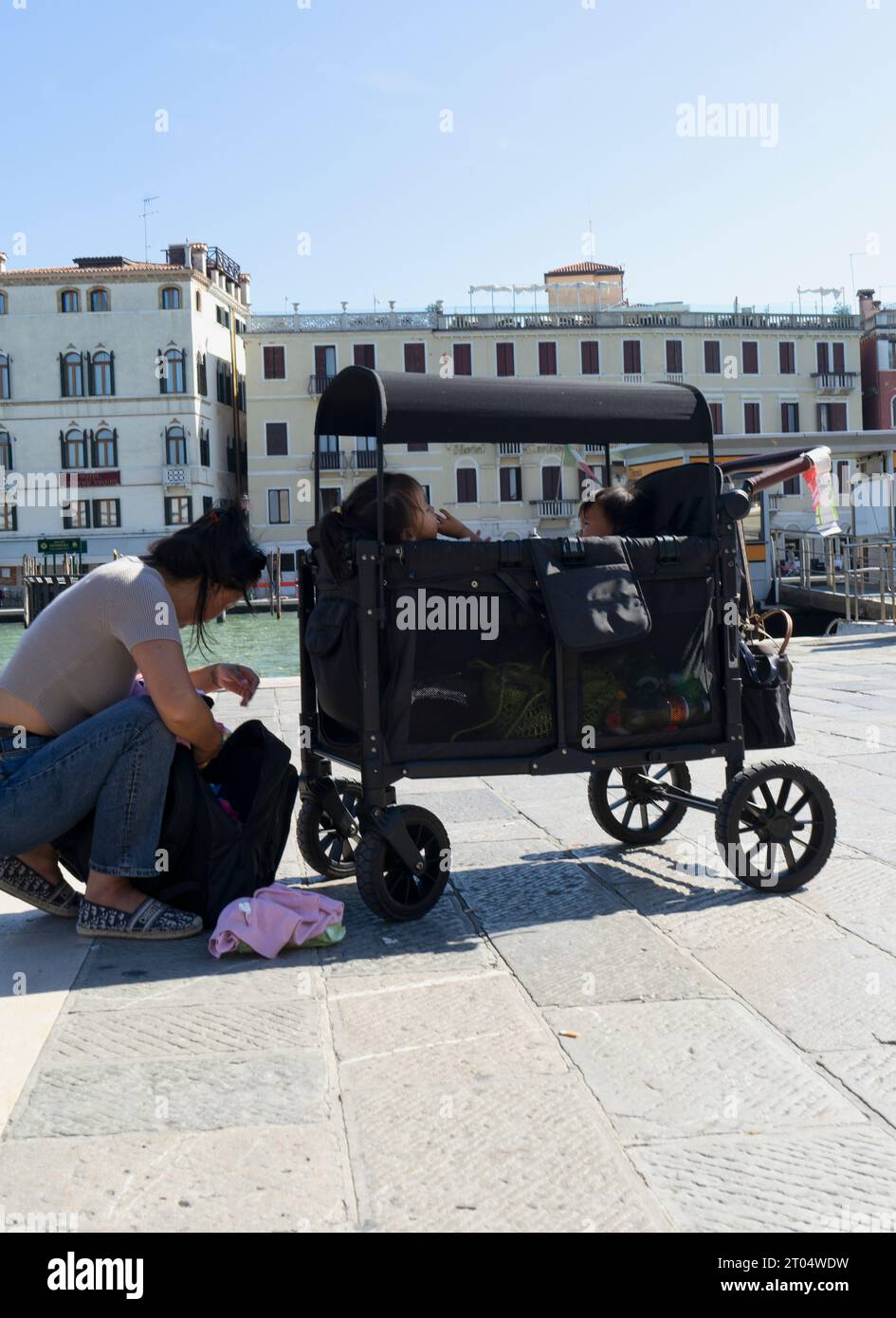 Una madre asiatica cammina con una carrozza e i bambini in vacanza a Venezia in una giornata di sole Foto Stock