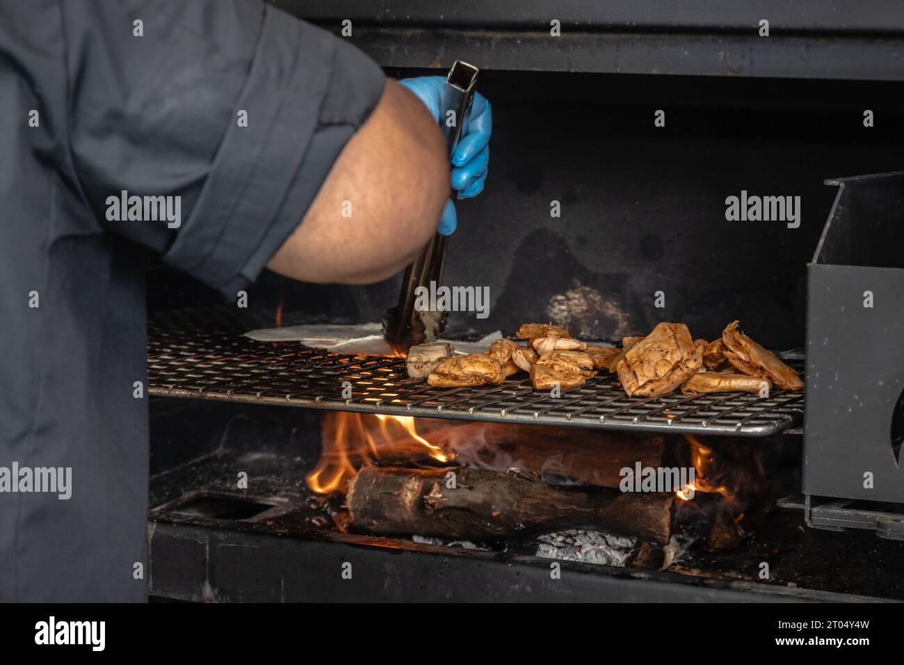 Nel caldo frizzante di una griglia di fuoco, una mano e un braccio girano abilmente il succulento pollo su una fiamma aperta, riempiendo l'aria con aromi appetitosi Foto Stock