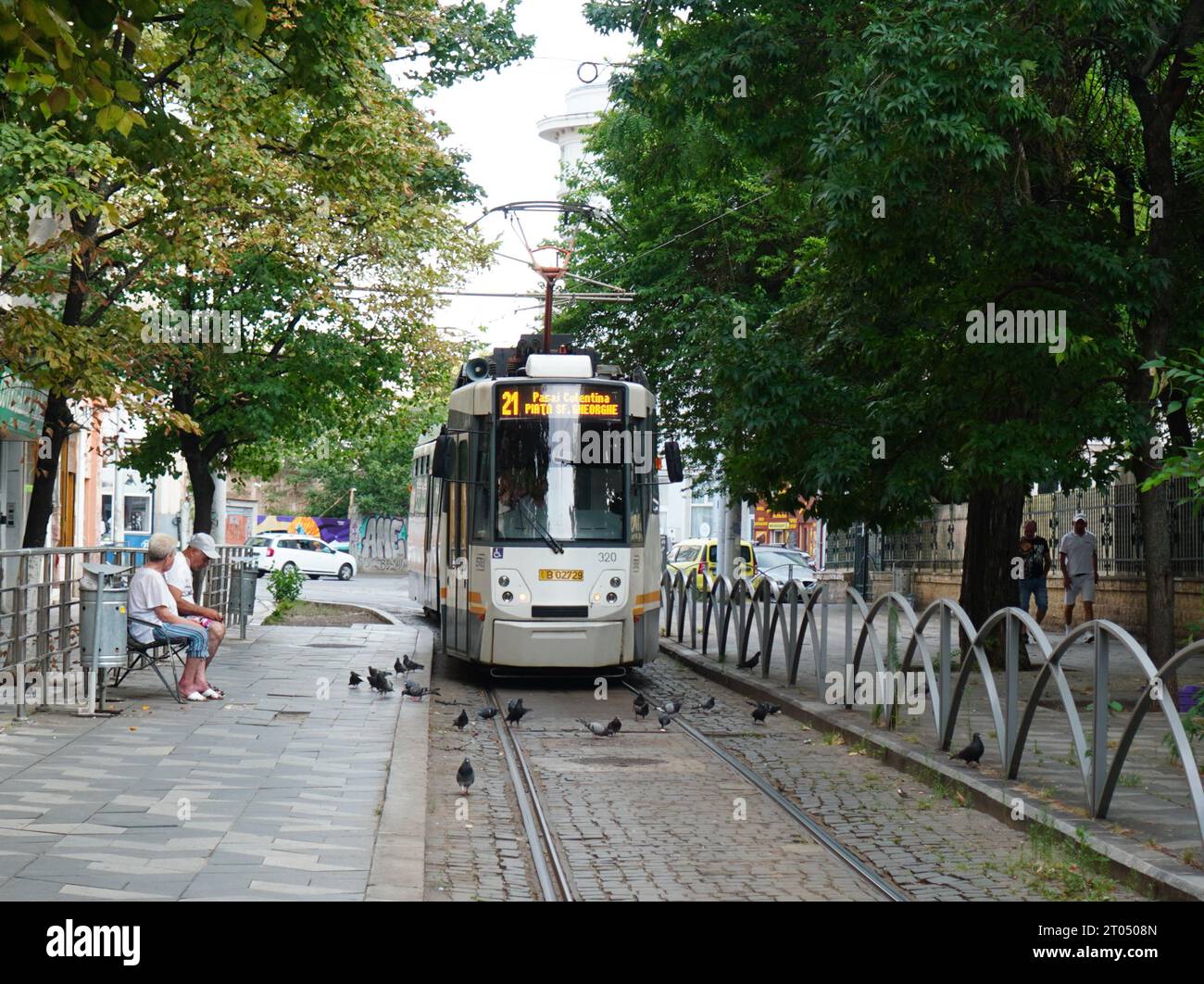 Tram che arriva alla stazione, persone in panchina in attesa e piccioni sul marciapiede a Bucarest, Romania, il 26 luglio 2023 Foto Stock