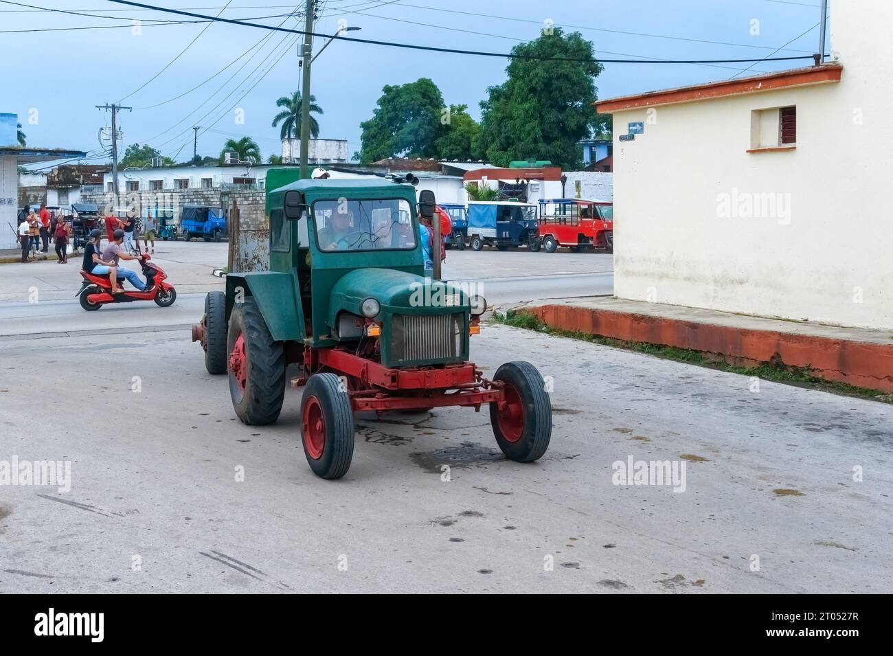Un uomo con una camicia militare guida un vecchio trattore agricolo in una strada cittadina.Santa Clara, Cuba, 2023 Foto Stock