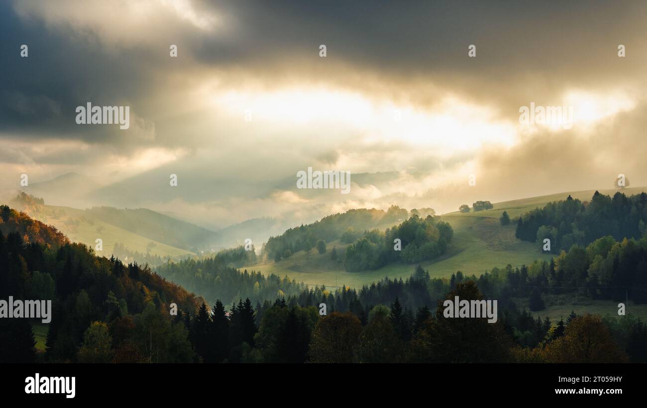 Paesaggio montuoso nebbioso autunnale con raggi del sole mattutino che brillano tra le nuvole. La regione di Orava in Slovacchia, Europa. Foto Stock