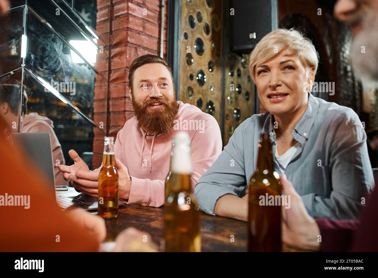 uomo barbuto eccitato che parla e condivide l'idea di colleghi di lavoro seduti in un pub dopo il lavoro Foto Stock