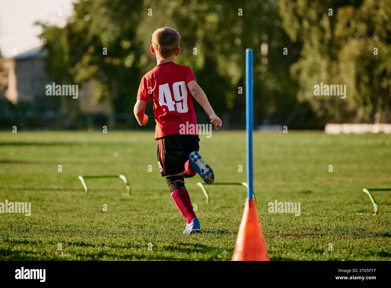 vista posteriore del bambino, giocatore di football in uniforme sportiva che corre, allenarsi, allenarsi con le patatine di calcio in movimento prima della partita sul campo di calcio. Foto Stock